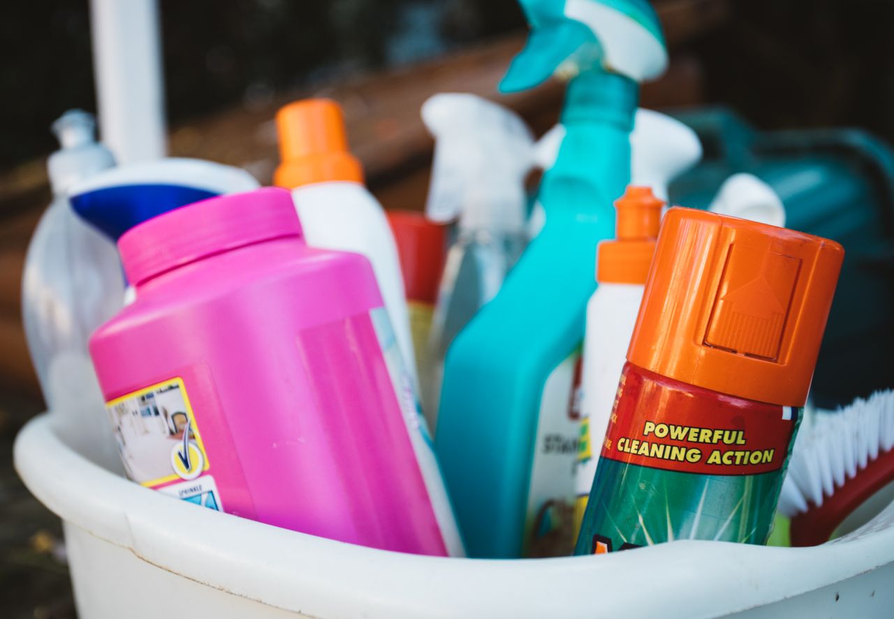 about-01 Close-up of assorted cleaning supplies in a bucket outdoors, showcasing various detergents and sprays.